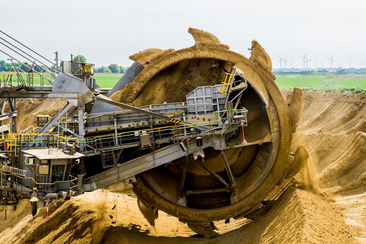 creative-03 A large bucket wheel excavator working in an open pit mine against a green landscape.