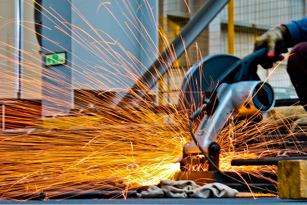Services-02 A worker operates a grinder cutting metal, creating a vibrant display of sparks in an industrial setting.