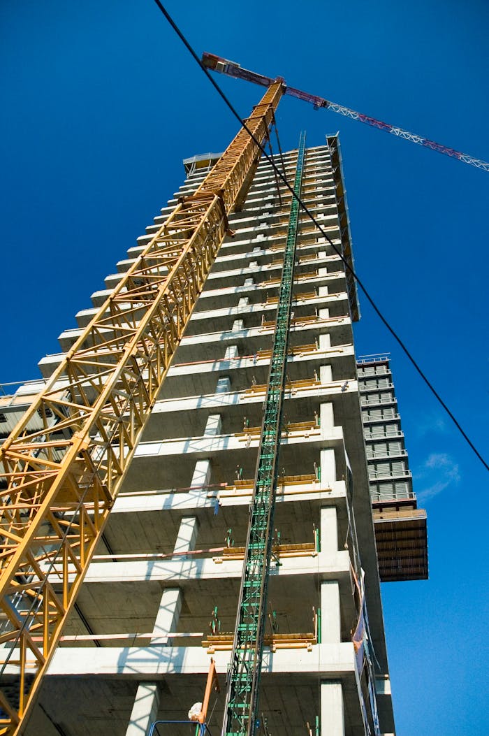 digital Low-angle view of skyscraper under construction with crane, clear blue sky.