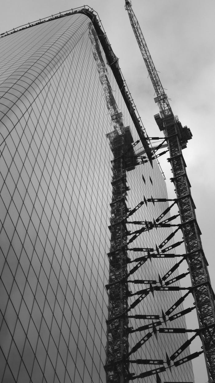 creative-03 Low angle view of a skyscraper under construction with cranes, captured in monochrome.